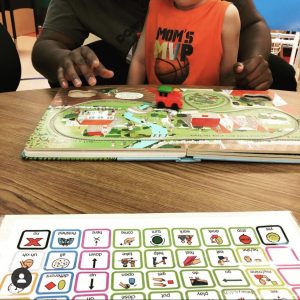 picture of core vocabulary communication board with prek student reading and playing with the "Busy Train" Book