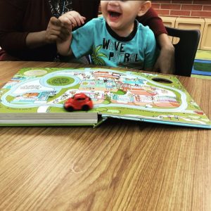 picture of prek student reading and playing with the "Busy Car" book