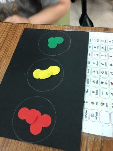 black construction paper rectangle with 3 white circles drawn down the center with red stickers in the top circle, yellow stickers in the middle and green stickers at the bottom